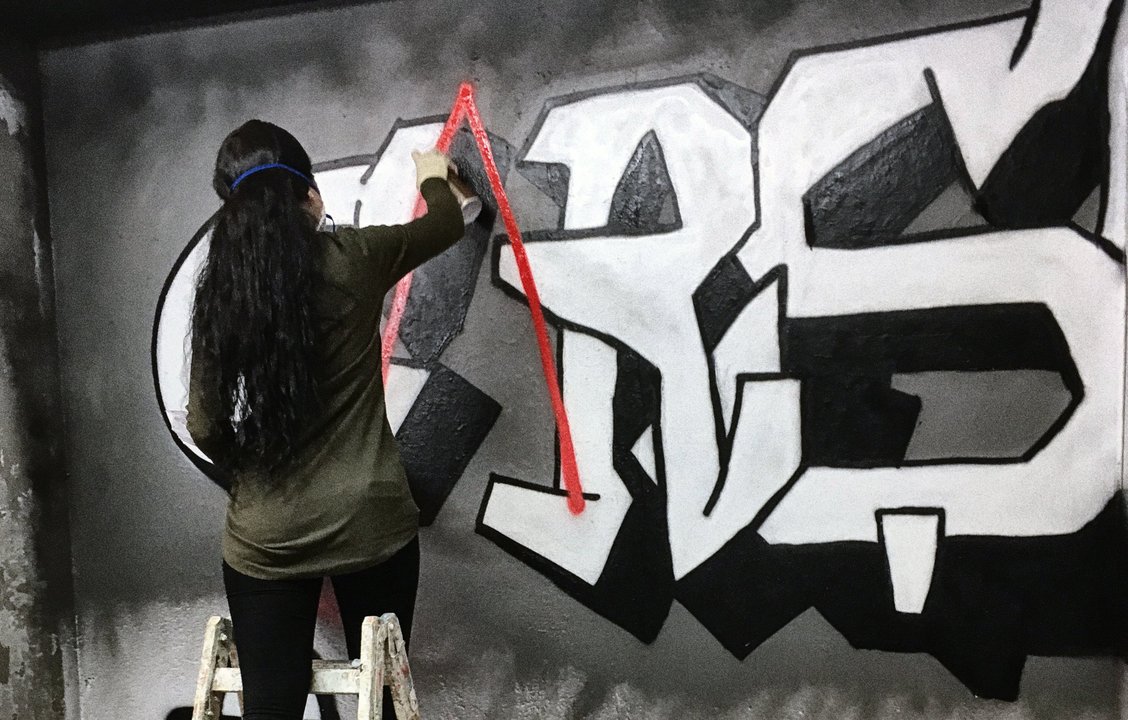 Junge Frau steht auf einer Leiter und sprayt an eine Wand