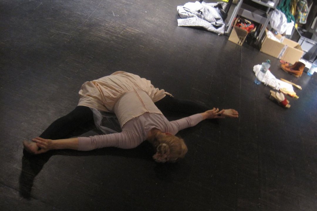 Frau liegt im Spagat auf dem Bauch auf dem Boden der Bühne