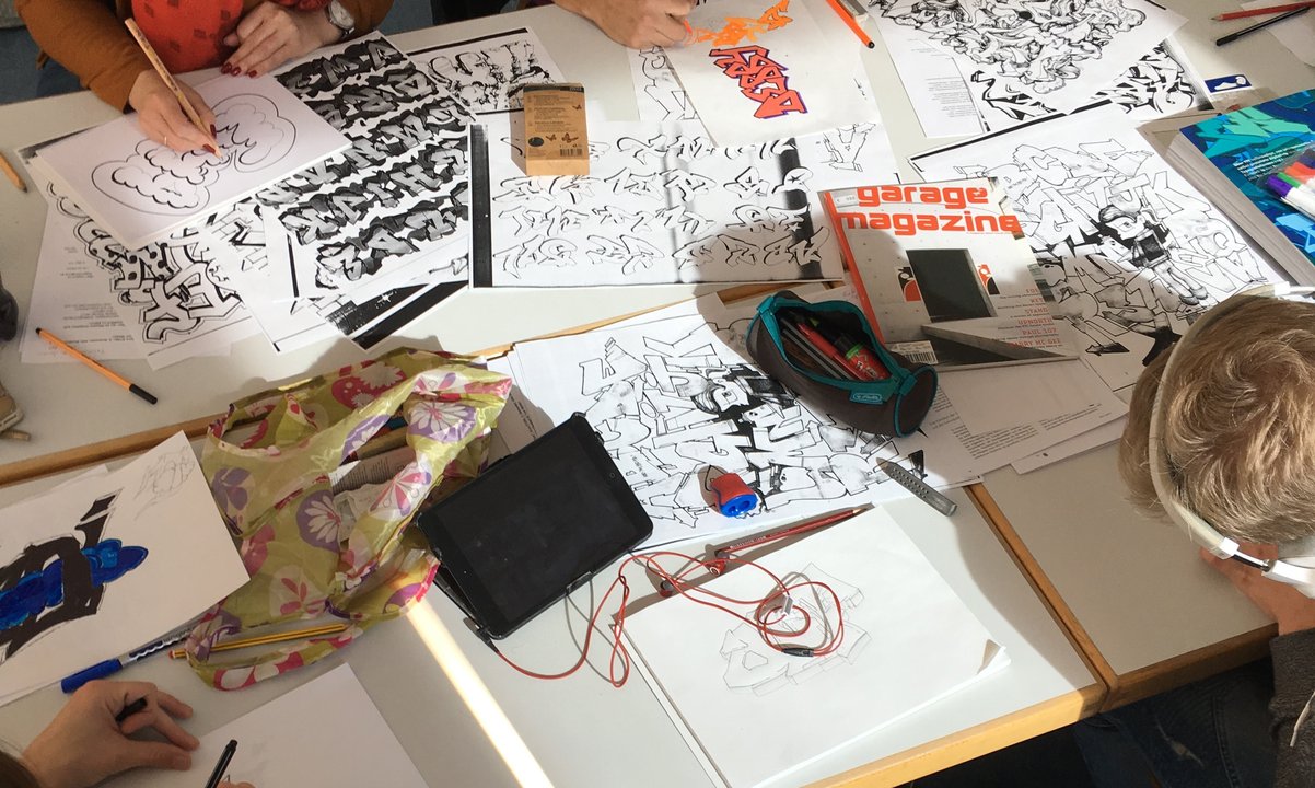 Mehrere Jugendliche sitzen an einem Tisch und zeichnen konzentriert