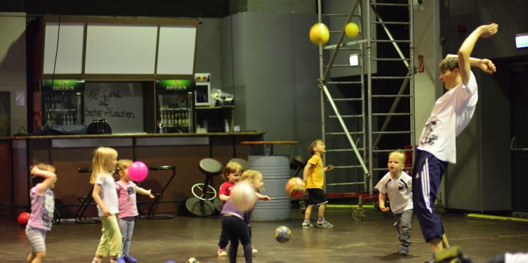 Ballspielende Kinder mit Erzieher in einer Halle mit Sprossenwand.