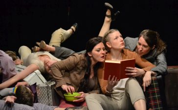 Theaterszene aus dem Theaterstück_Frauen sitzen kreuz und quer auf einem Fleck mit Koffern
