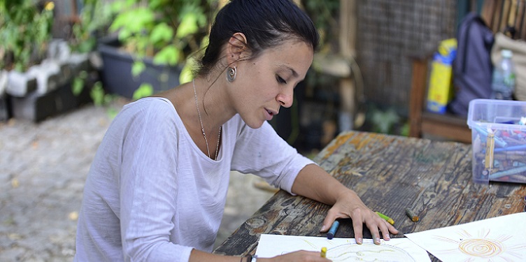 Junge Frau schreibt an einem Holztisch unter freiem Himmel